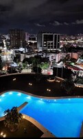A nighttime view of a cityscape with a lit swimming pool in the foreground.