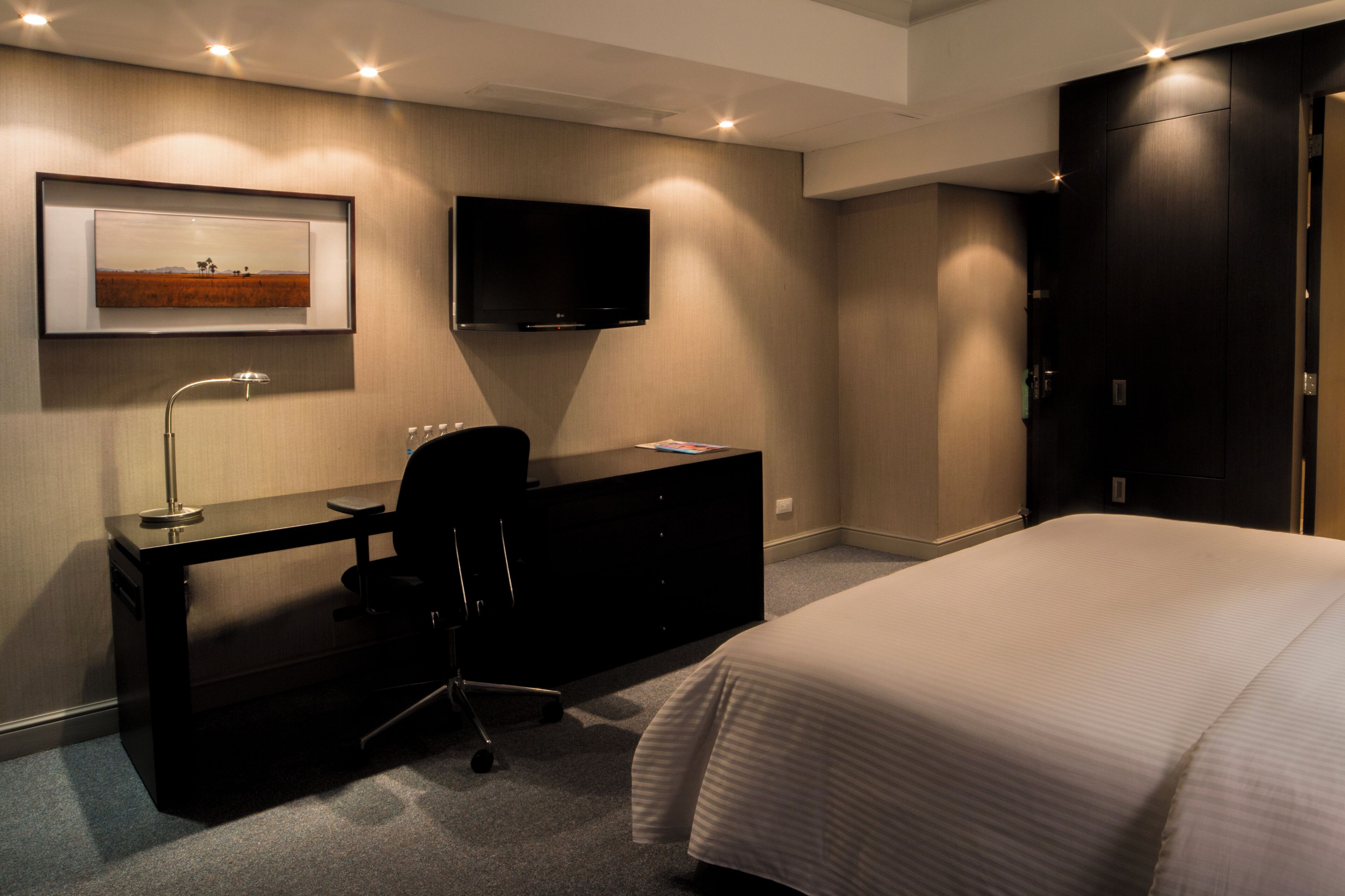 A hotel room with a bed, a desk with a chair, a television, and a framed picture on the wall.