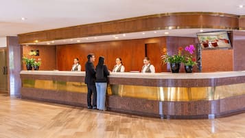 Eine Hotelrezeption mit Marmorarbeitsplatte, Holzvertäfelung und Zimmerpflanzen.