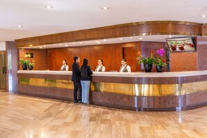 Een hotel receptiebalie met een marmeren aanrechtblad, houten lambrisering en kamerplanten.