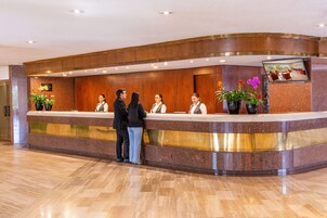 A hotel reception desk with a marble counter, wooden paneling, and potted plants.