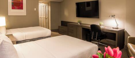 A hotel room with two beds, a desk, a chair, a TV, and a window with blinds.