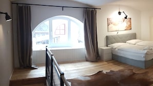 A bedroom with a large bed, a wooden floor, a mirror, and a view of the outside. - Sobieski Apartments Historic City (Vienna)
