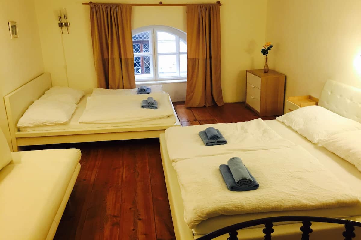 A room with two single beds, a wooden dresser, a small table, and a window with curtains.