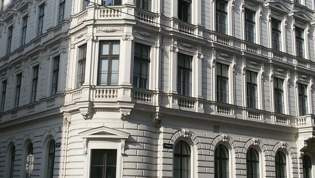 Un immeuble à plusieurs étages présentant des éléments d’architecture classique, notamment des colonnes richement décorées et des moulures ornementales.