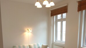 Un salon avec un canapé à rayures, un petit pouf, une table basse ronde et une lampe fixée au mur.