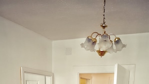 Um quarto com assoalho de madeira, um sofá bege, uma mesa de vidro e um lustre.