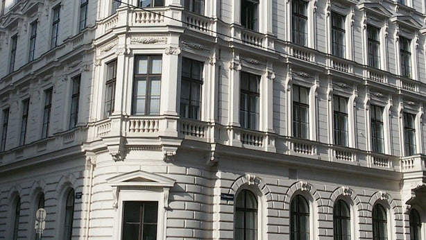 Um edifício de vários andares com características arquitetônicas clássicas, incluindo colunas elaboradas e molduras decorativas.