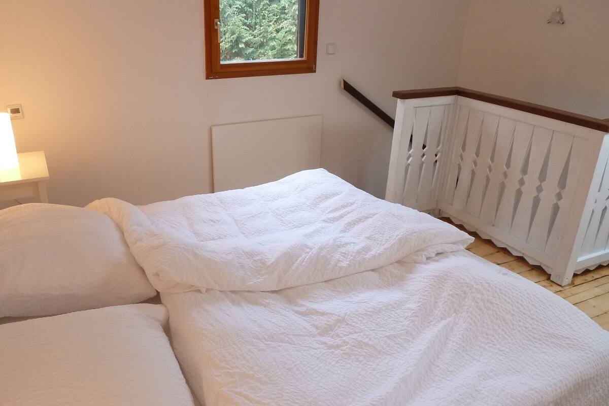 A bedroom with a bed, a nightstand, a window, and a white railing.