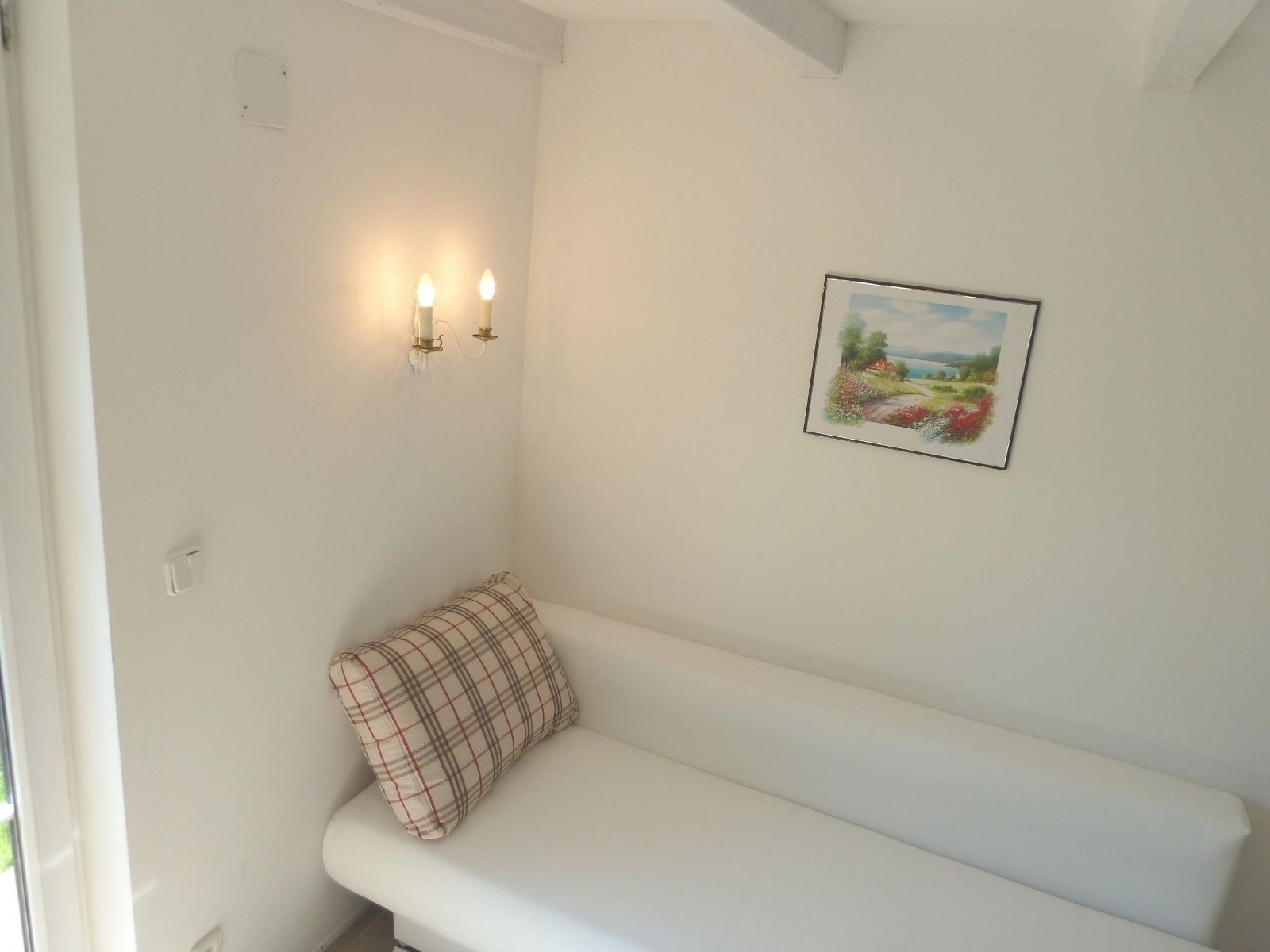 A white bench with a plaid pillow, two wall-mounted lights, and a framed landscape painting.