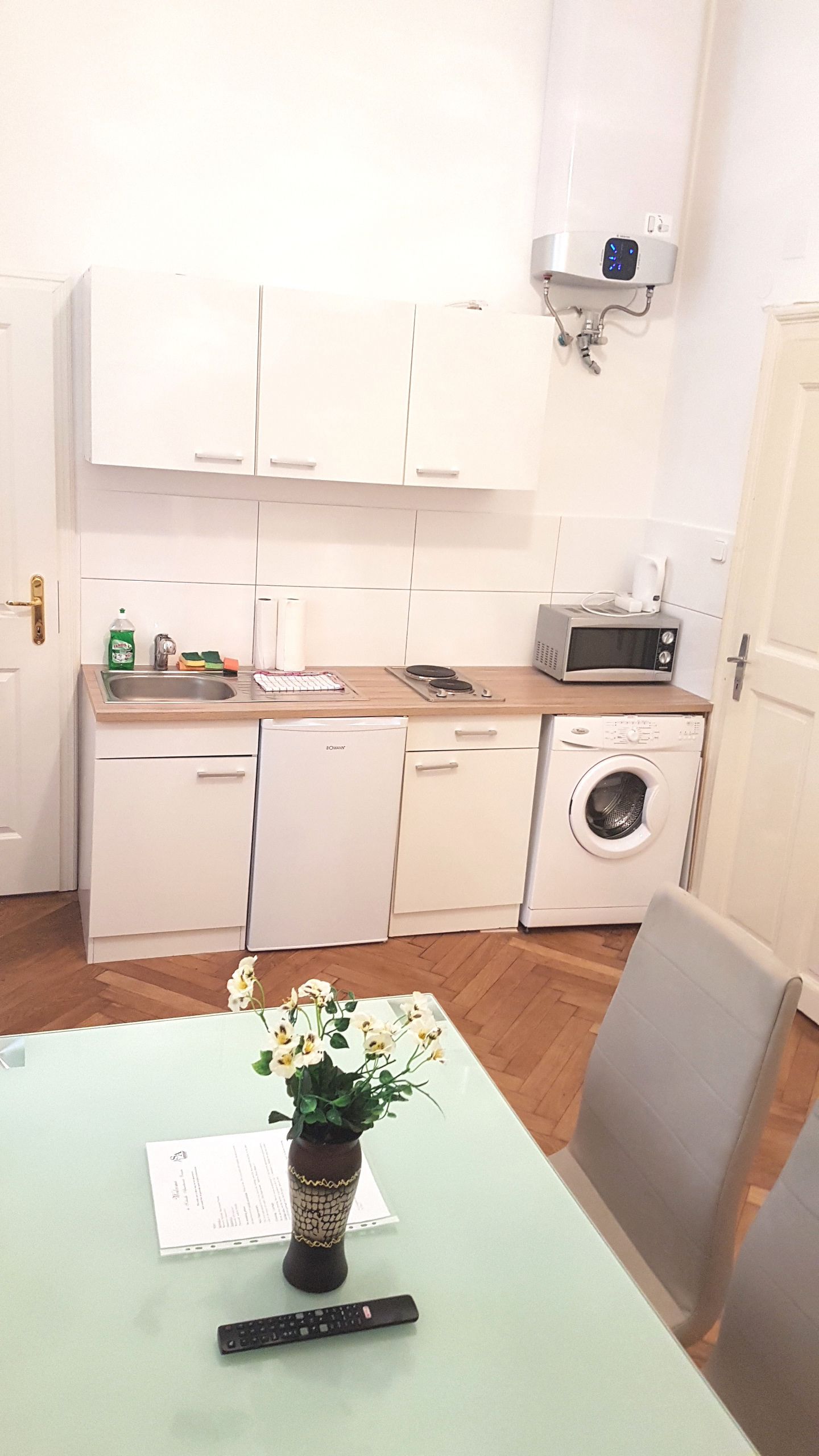 A compact kitchen with white cabinets, a microwave, a washing machine, and a sink.