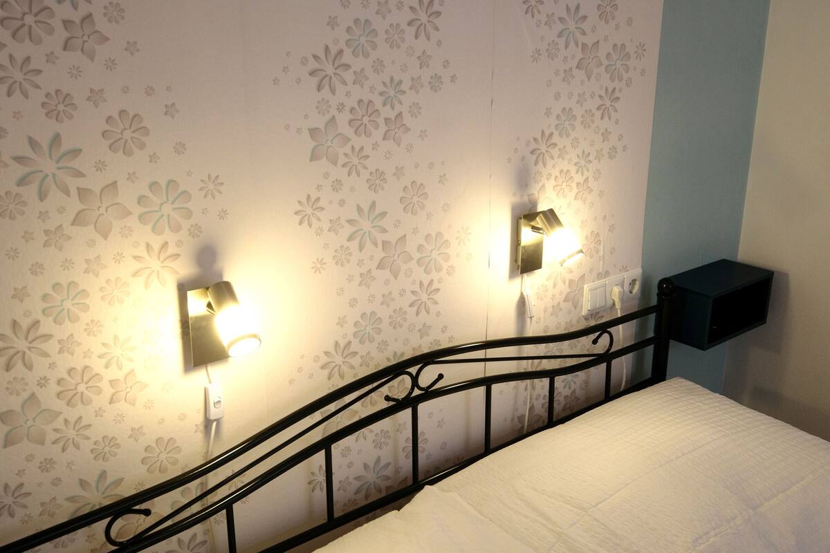 Un dormitorio con cama, luz empotrada en la pared y toma corriente.