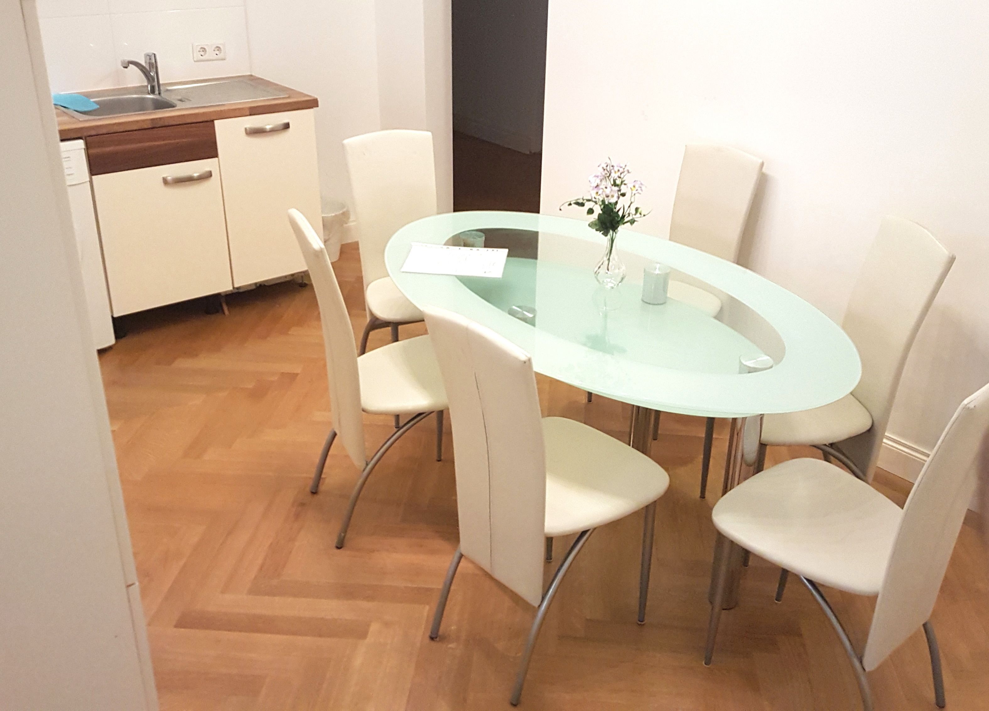 Eine moderne Küche mit Spüle, Schränken und einem Essbereich mit Glastisch und Stühlen.