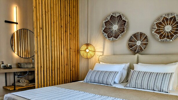 A modern bedroom with a large bed, a wooden slat wall, a round mirror, and three decorative wall pieces.