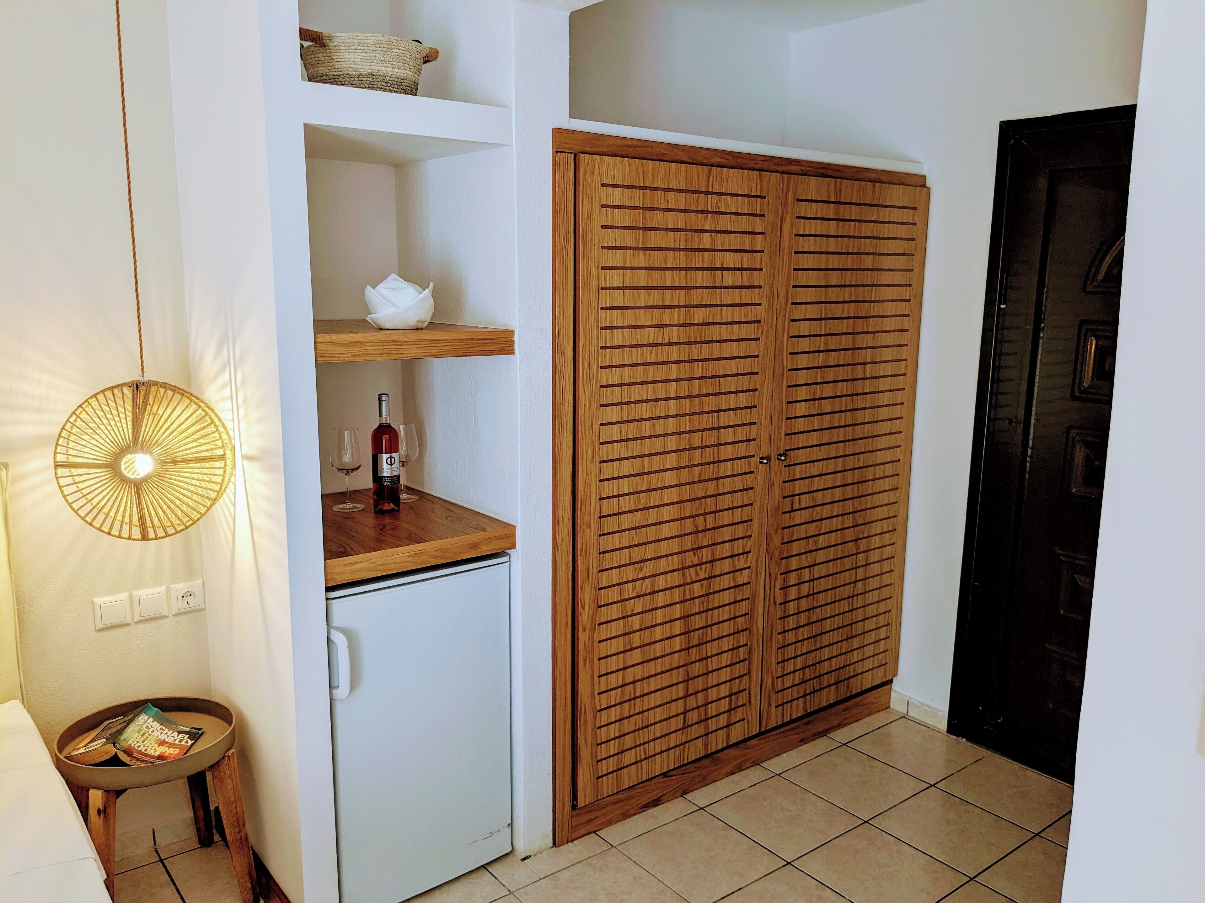 Een compacte kamer met een houten garderobe, een klein tafeltje met een tijdschrift en een hanglamp.