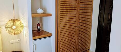Een compacte kamer met een houten garderobe, een klein tafeltje met een tijdschrift en een hanglamp.