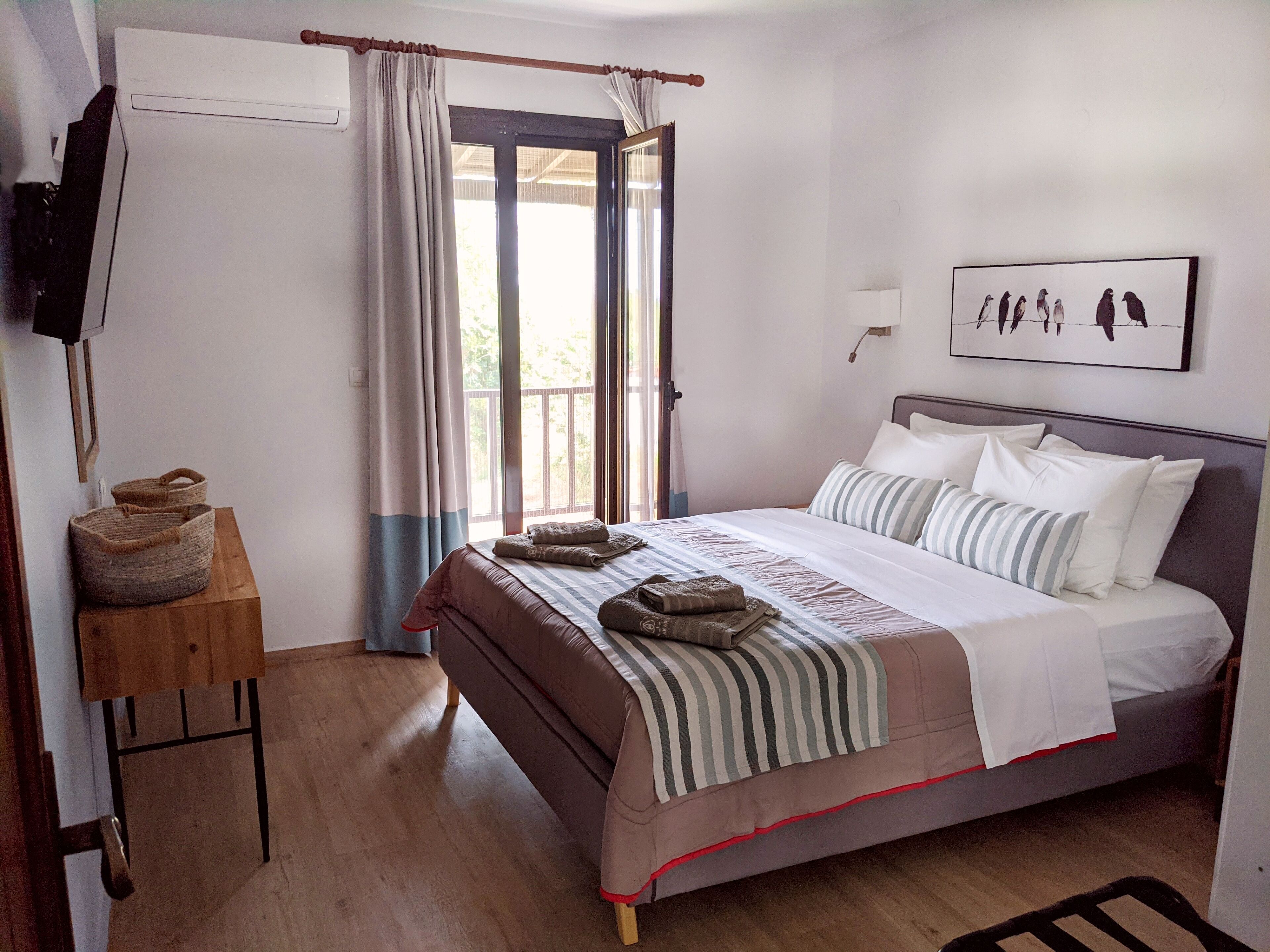 A bedroom with a bed, pillows, a bedside table with a lamp, a window with curtains, and a wall-mounted artwork.