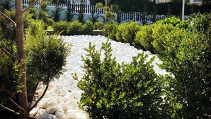 A landscaped garden with a white pebble path, green shrubs, and a tree.