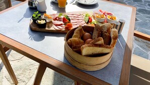 A breakfast table with a variety of foods including bread, eggs, and meats, along with a cup of coffee and a glass of orange juice.