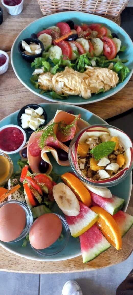 A table with a variety of food items including a salad, a fruit bowl, and a plate with eggs and a drink.
