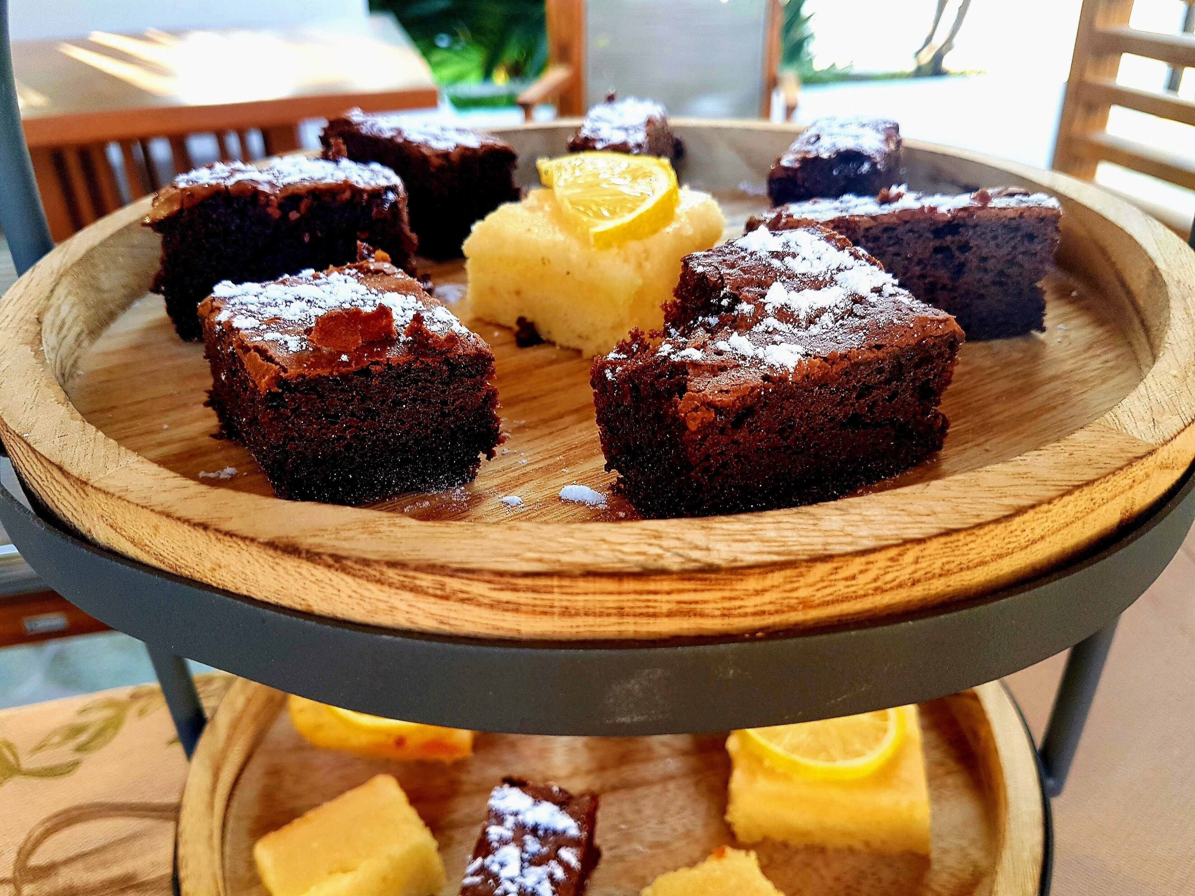Uma bandeja de madeira com vários pedaços de bolo escuro e uma porção de sobremesa amarela.