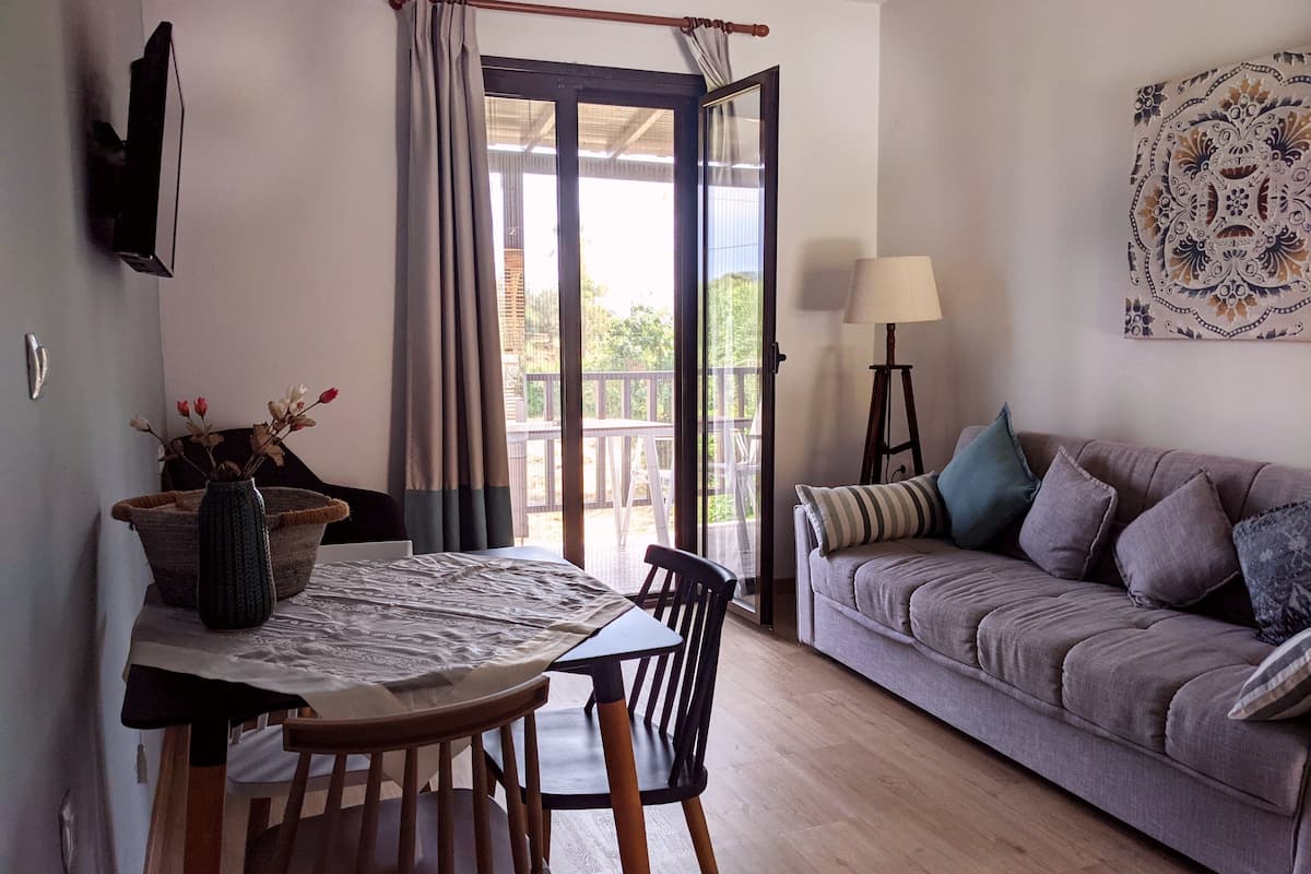 Ein Zimmer mit Esstisch, Stühlen, einer Couch, einer Lampe und Blick durch eine Glastür.