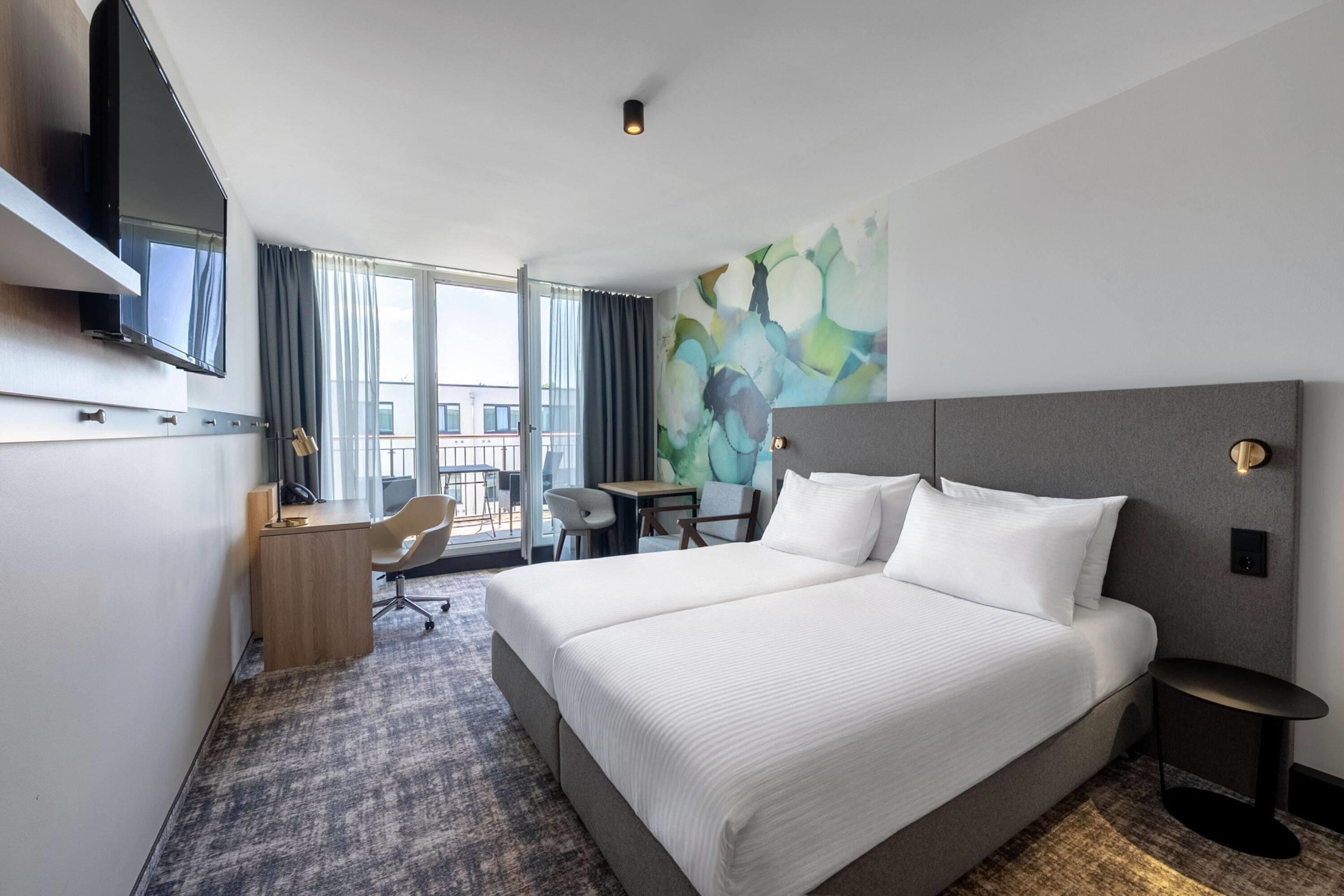 Habitación de hotel con una cama grande, un escritorio, una silla, un televisor de pantalla plana y vistas al exterior.