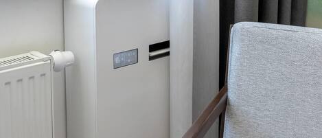 Una habitación moderna con un radiador blanco, un panel de control y una butaca tapizada de color gris.