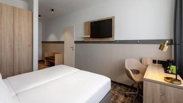 A hotel room with a bed, a desk, a chair, a TV, and a wardrobe.