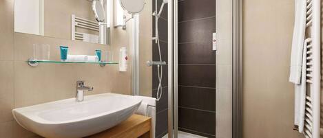 Un baño moderno con un lavamanos grande de color blanco, un estante de vidrio, un espejo y una ducha con mampara de vidrio.