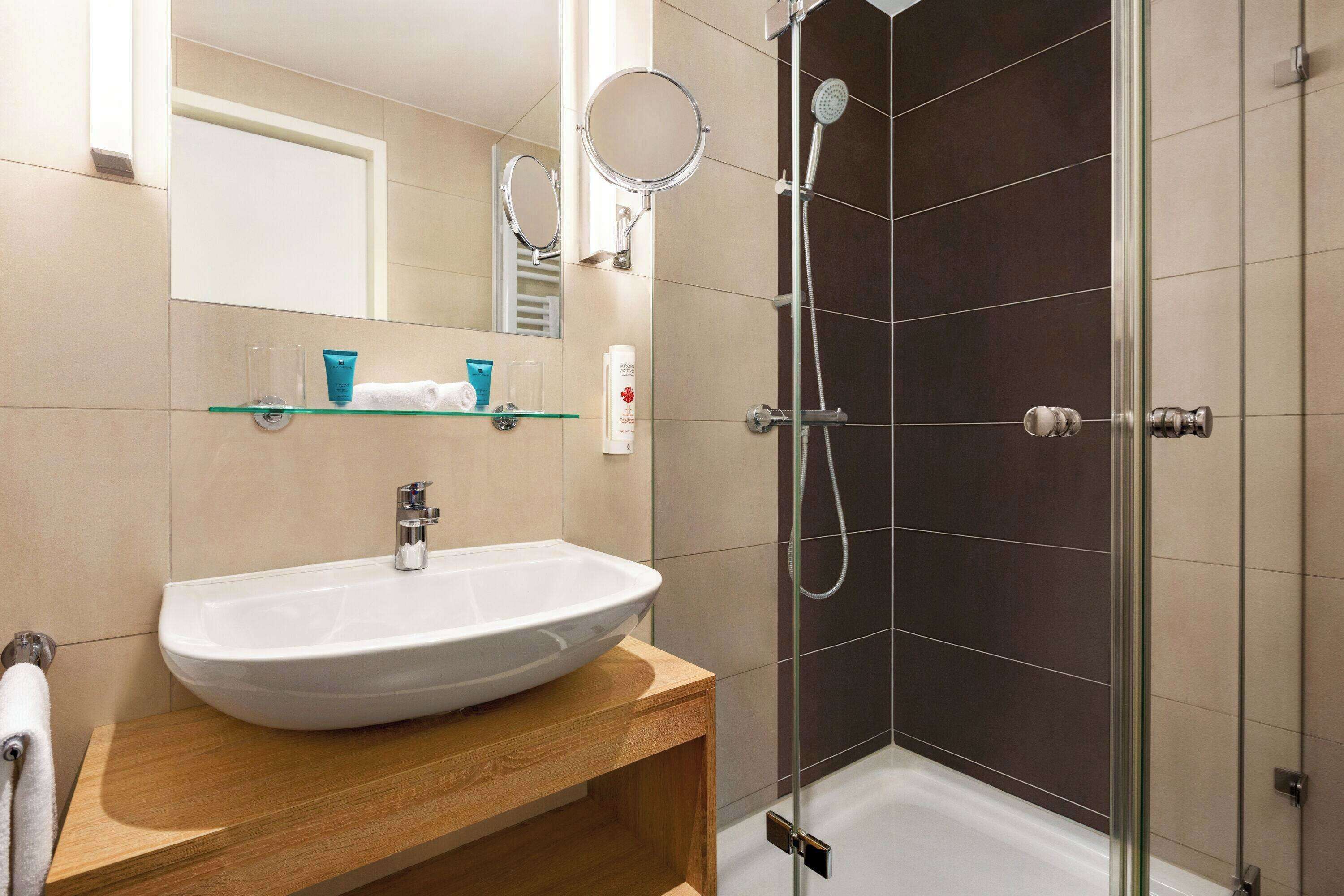 Ein modernes Badezimmer mit einem weißen Waschbecken, einer Duschkabine aus Glas und einem Spiegel über dem Waschbecken.