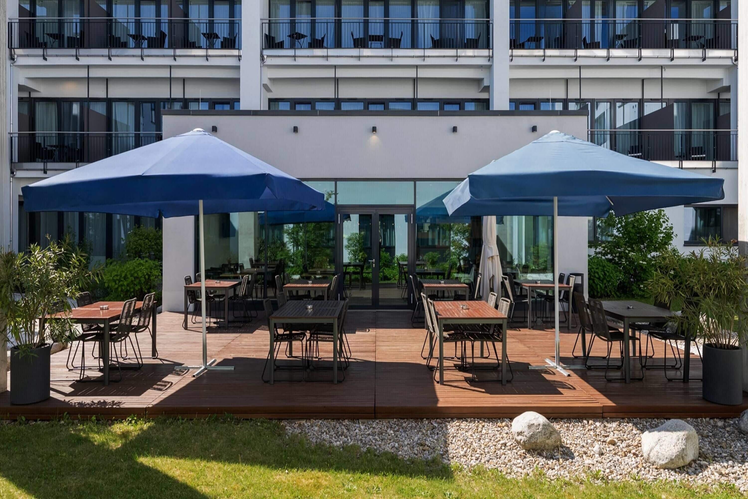 An outdoor patio with tables and chairs, large umbrellas, and potted plants.