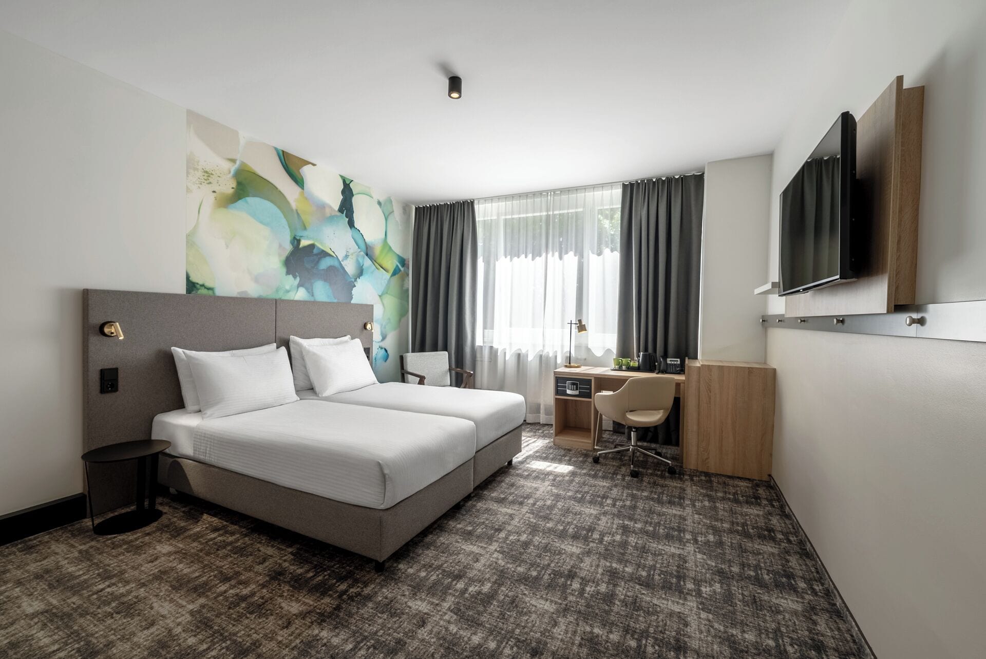 A hotel room with a large bed, a desk, a chair, a TV, and a window with curtains.