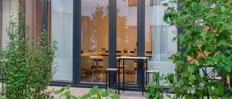 A modern building with large glass doors and a patio area with outdoor seating.