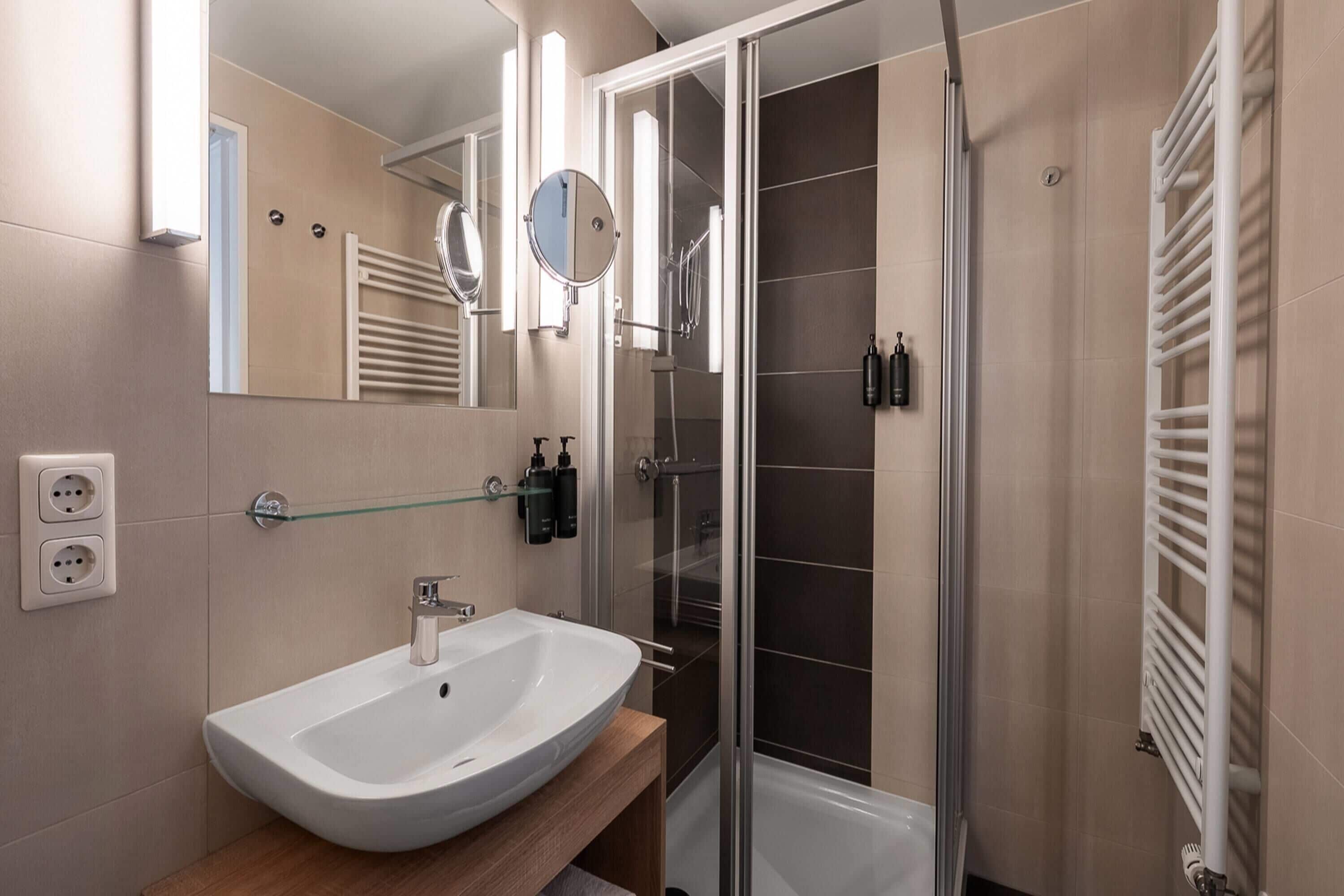 A modern bathroom with a white sink, glass shower enclosure, and a towel rack.