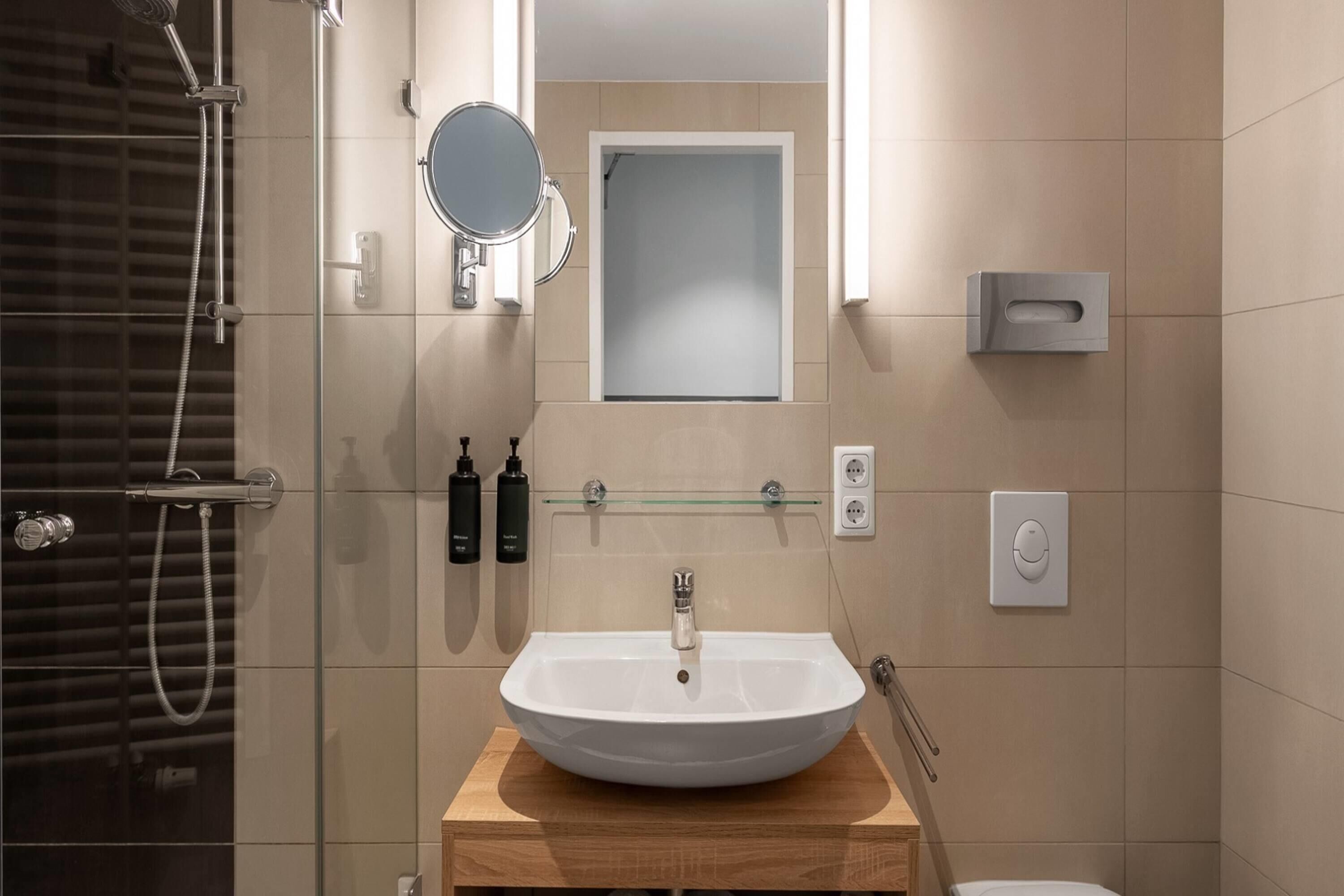 A modern bathroom with a glass-enclosed shower, a white sink on a wooden vanity, and a mirror above the sink.