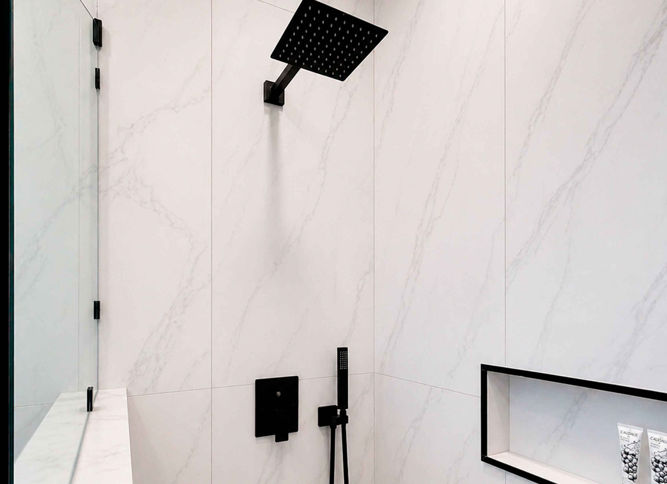 A modern bathroom with a marble wall, a black showerhead, a handheld shower, and a framed picture on the wall.