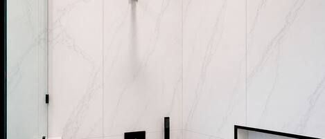 A modern bathroom with a marble wall, a black showerhead, a handheld shower, and a framed picture on the wall.