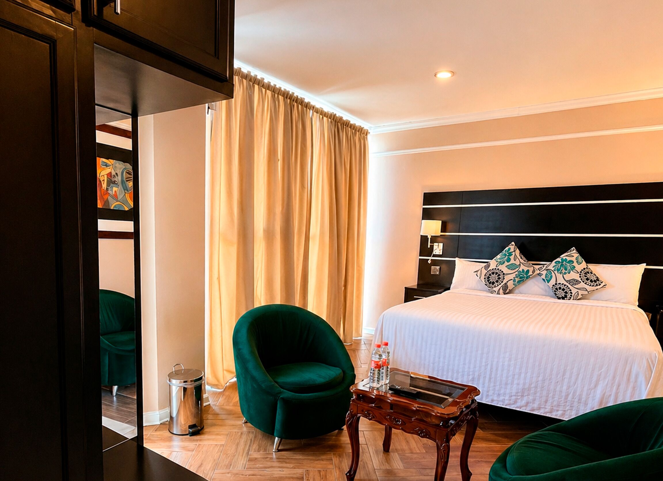 Ein Hotelzimmer mit einem Bett, grünen Sesseln, einem kleinen Tisch und einem Mülleimer.