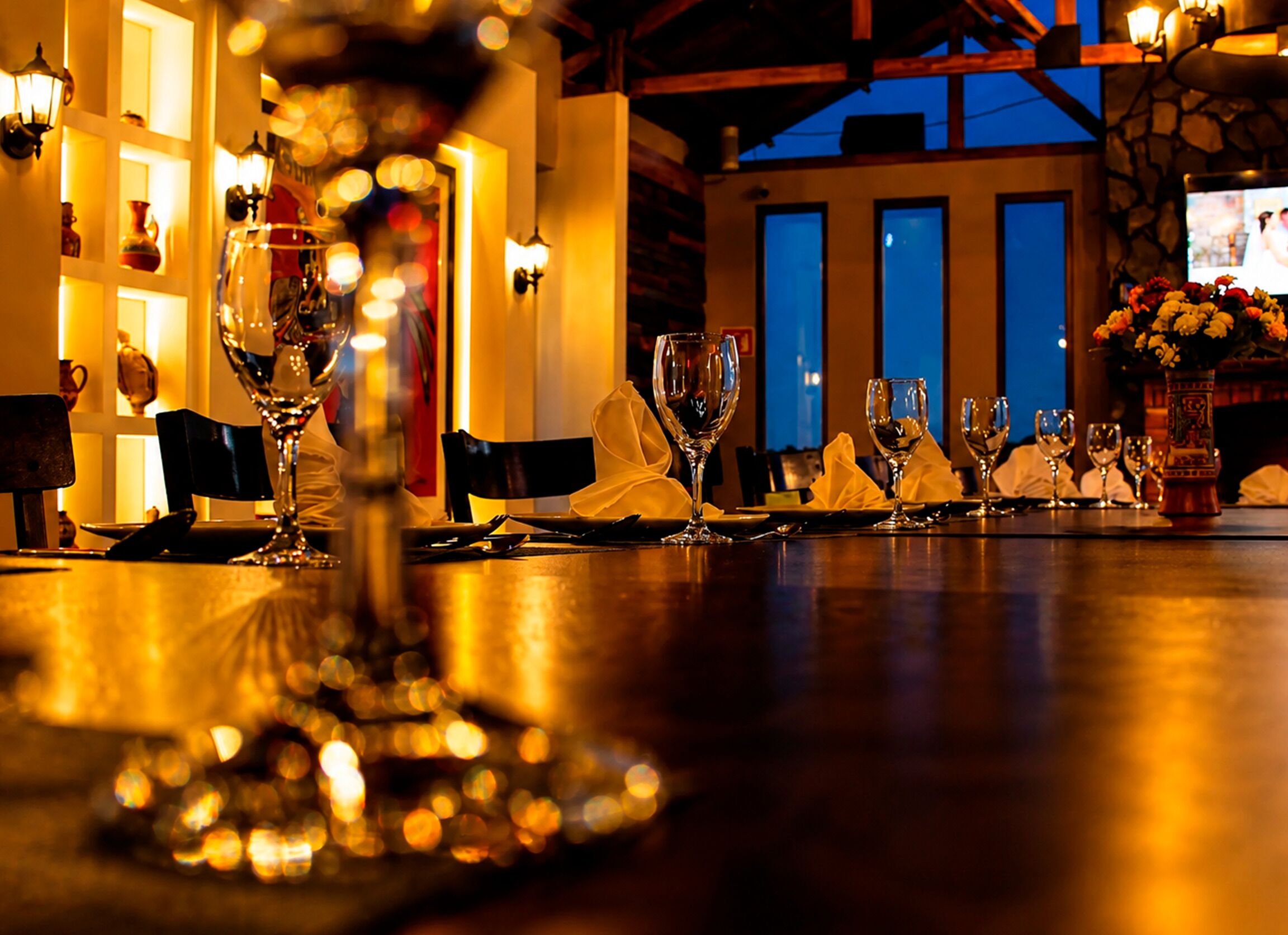 Zona de bar con varias copas de vino y una botella, una mesa con un jarrón de flores y vistas al exterior a través de una ventana.