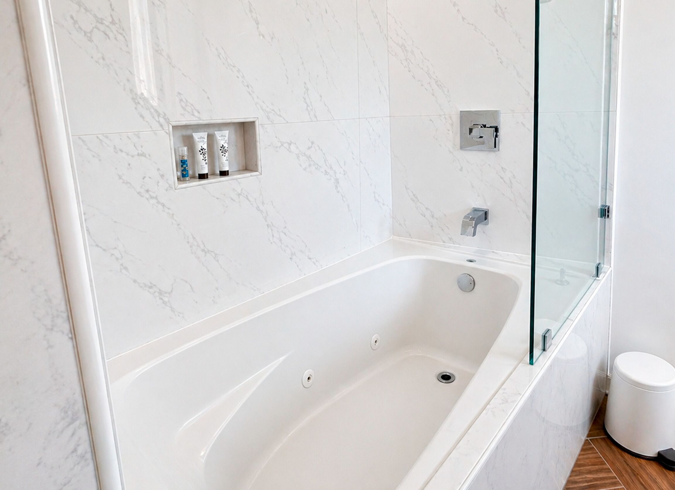 A modern bathroom with a marble wall, a glass-enclosed shower, and a built-in shelf with toiletries.