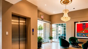 A modern lobby with an elevator, a digital exit sign, a chandelier, and a colorful abstract painting.