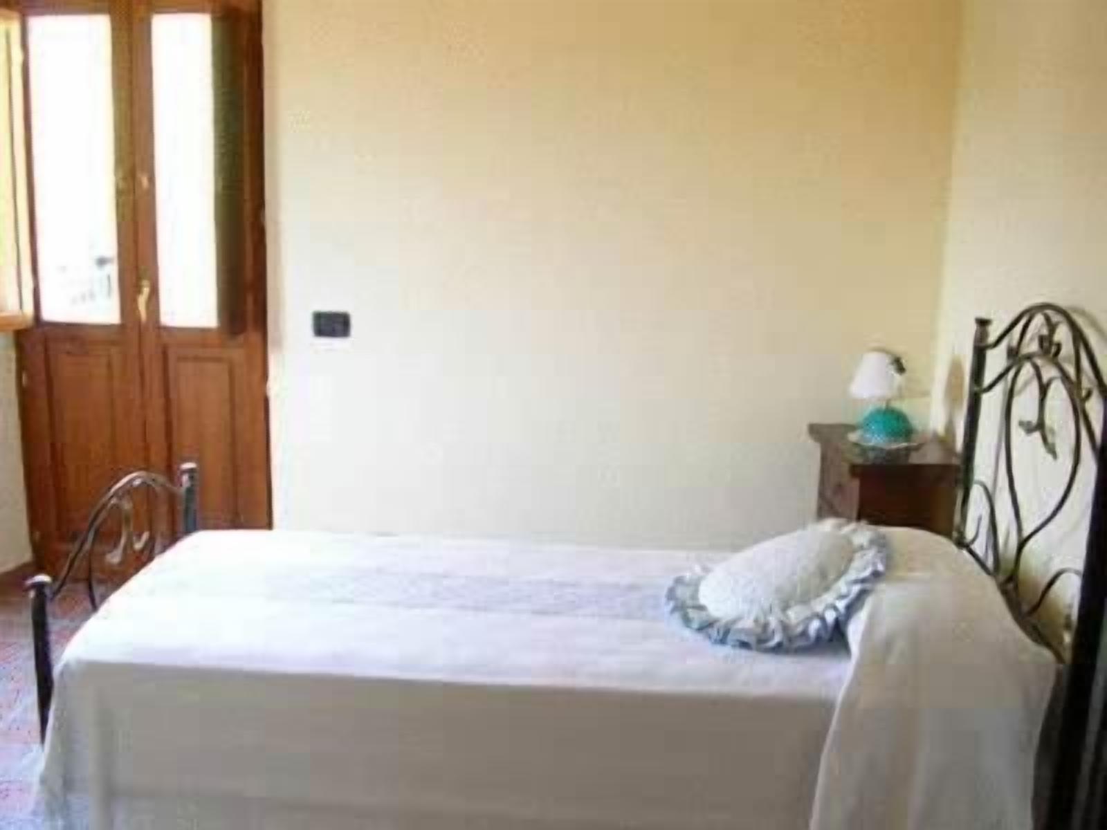 Una camera da letto con un letto, una porta in legno, un comodino con una lampada e un poggiatesta in metallo.