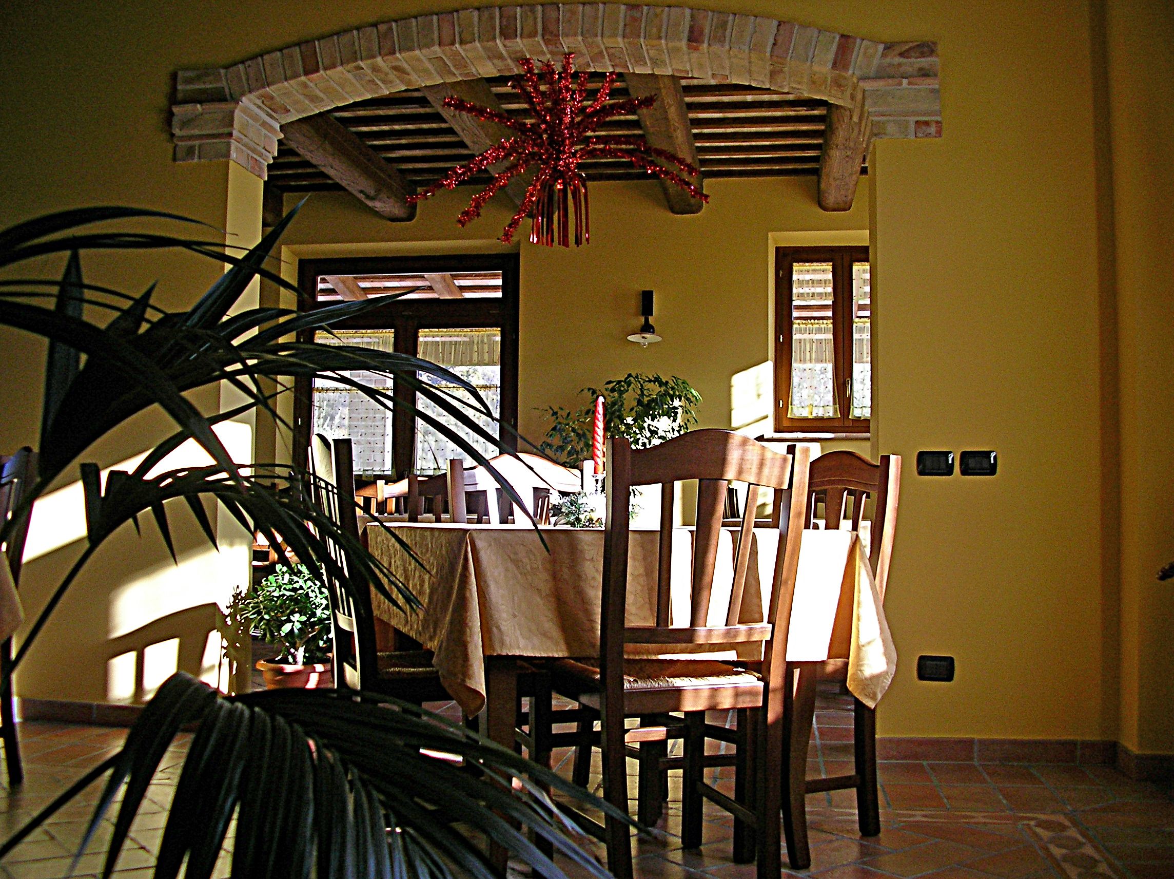 A dining area with a table set for two, wooden chairs, a potted plant, and a decorative red ornament.