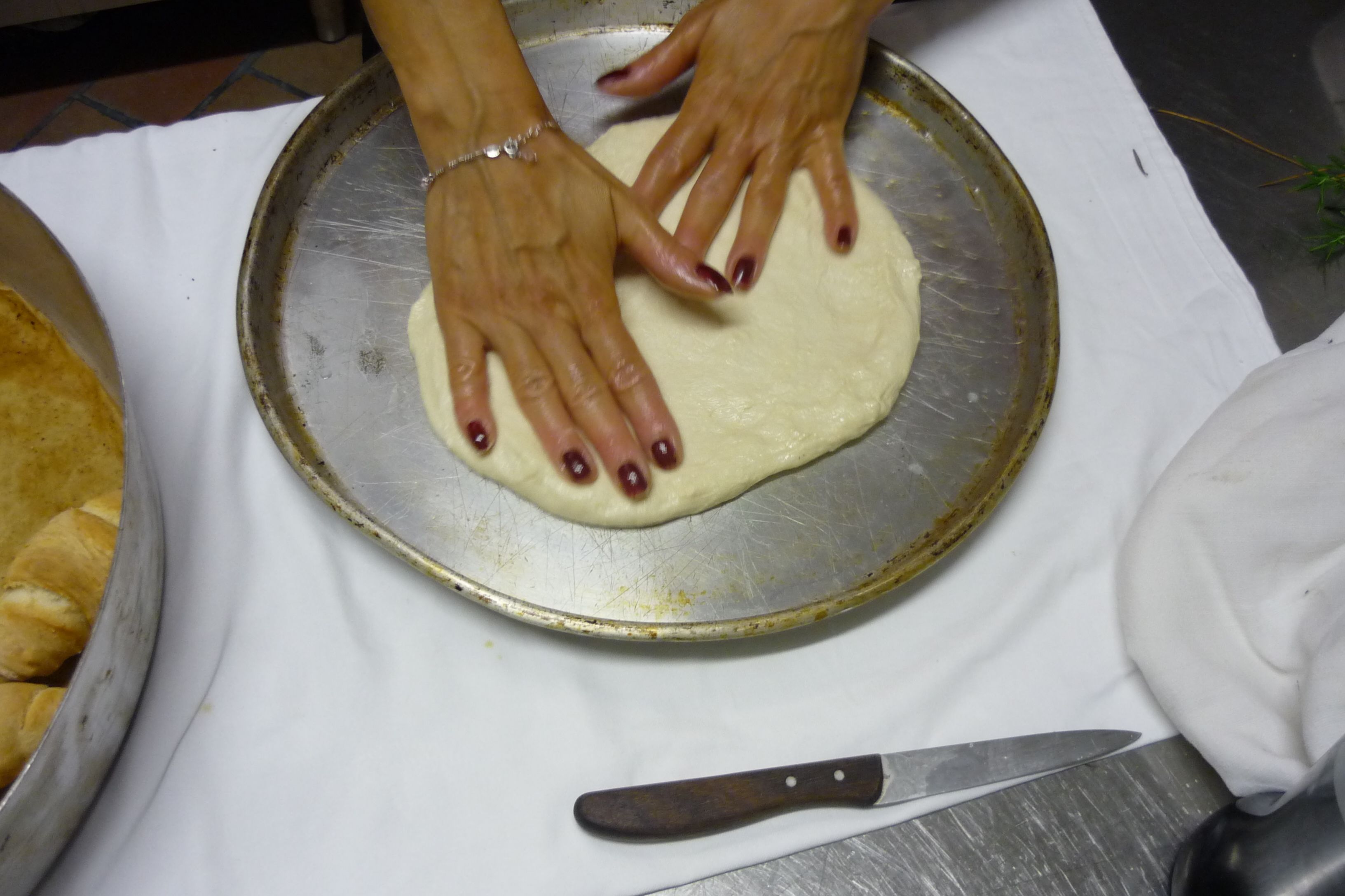 Hands shaping dough on a metal tray.