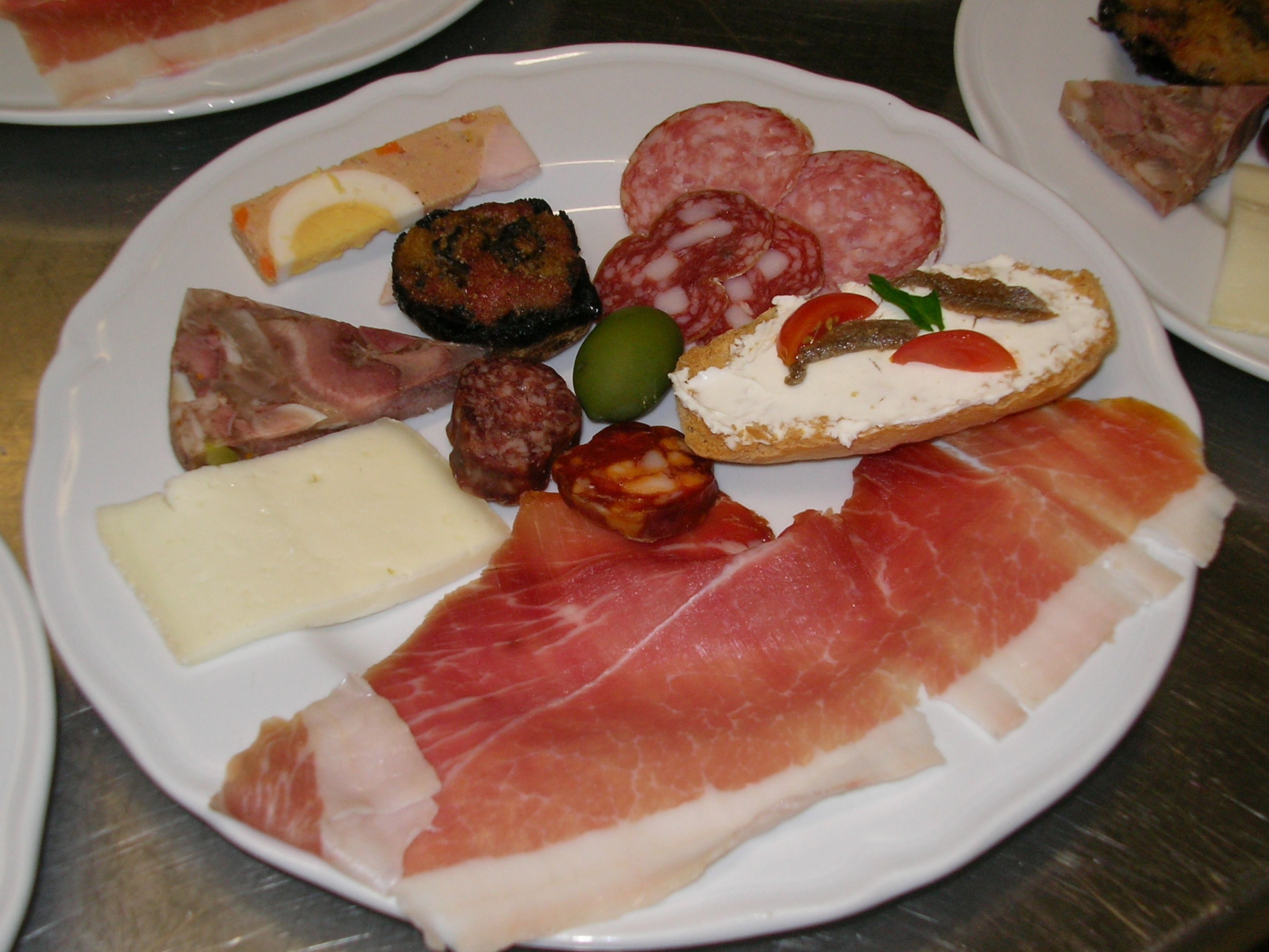 Une assiette garnie de différents types de charcuteries, de fromages et d’olives.