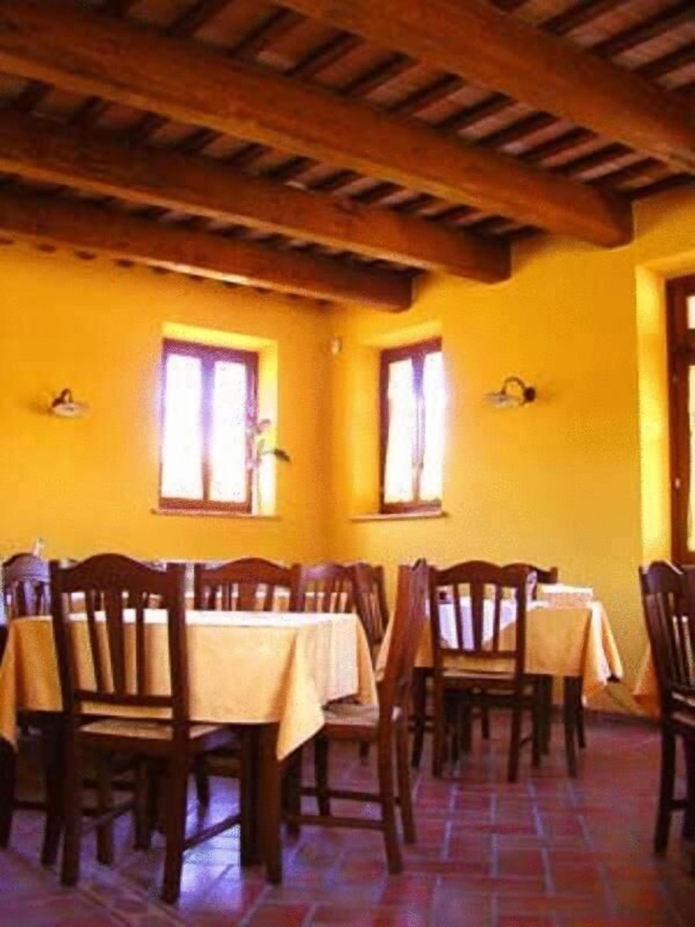 Un comedor con mesas y sillas de madera, paredes amarillas y ventanas grandes.