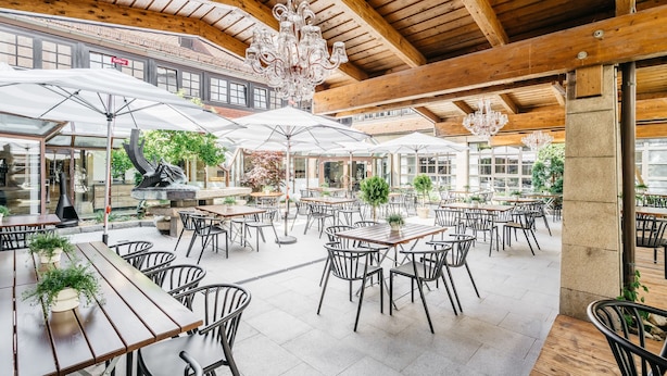 Un área de comedor al aire libre con mesas y sillas de madera, rodeada de sombrillas grandes.