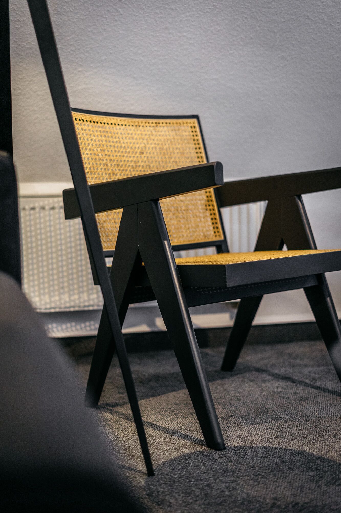 Una silla con respaldo y asiento de mimbre, ubicada frente a una pared blanca.