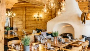 Un interior rústico de madera con una gran mesa de comedor rodeada de sillas de madera, una chimenea y lámparas colgantes.